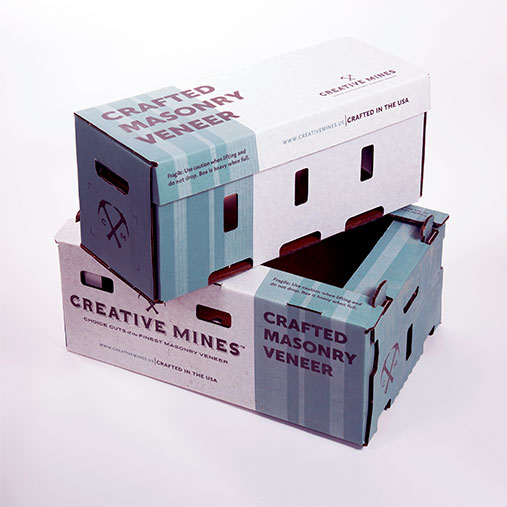 Two stacked rectangular boxes from Creative Mines labeled 'Crafted Masonry Veneer.' The boxes are white with blue-green vertical accents and bold maroon text. Both boxes have die-cut handles and ventilation slots. The top box is fully closed while the bottom one has an open flap, revealing part of the interior. Branding includes the Creative Mines logo and the phrase 'Crafted in the USA.