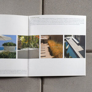 Open Syndecrete brochure laid flat on a concrete tile surface. The left page features a row of six square images showcasing modern architectural applications of Syndecrete products: a bathroom sink, an outdoor umbrella, planters, garden edging, a walkway, and a poolside installation. The right page contains informational text about Syndecrete’s sustainable, cement-based material solutions.