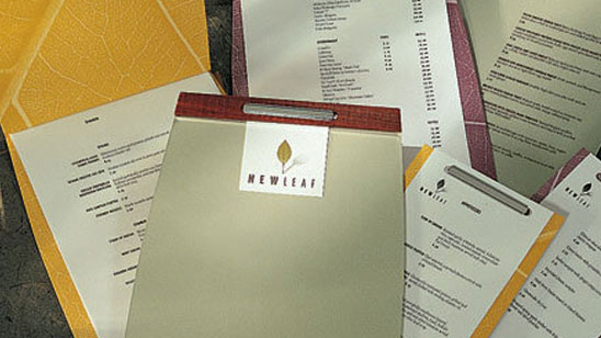 NewLeaf branded stationery and menus arranged in a flat lay. The logo features a gold leaf icon above the word “NEWLEAF” in modern serif lettering, printed on neutral and earth-toned materials.