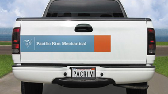 Rear view of a white pickup truck with a “Pacific Rim Mechanical” logo decal on the tailgate, featuring blue and orange color blocks and a stylized “PRM” dot design. Custom license plate reads “PACRIM.”