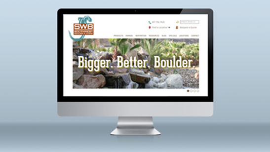 Desktop computer displaying the SWB Landscape Materials website homepage, featuring a banner with the slogan “Bigger. Better. Boulder.” over a background of large decorative landscape rocks.