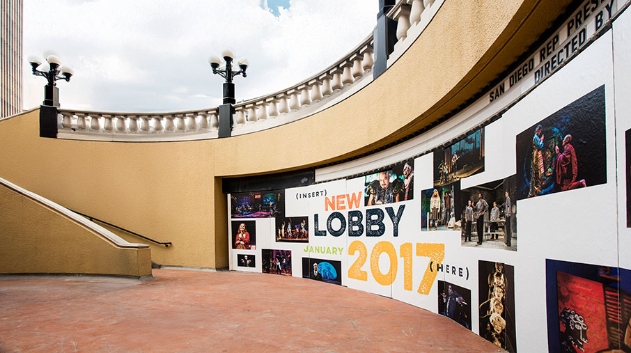 Outdoor view of the San Diego REP Theatre showing a large curved barricade wall with promotional signage announcing a "New Lobby January 2017." The signage includes theatrical photos of past performances and bold typography. The area is paved with reddish concrete and bordered by a beige wall and railing above.