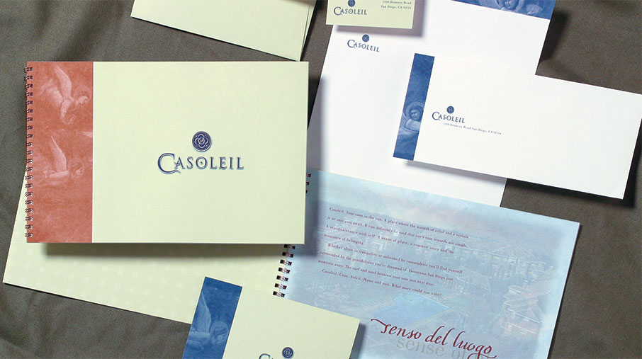 Branded stationery and marketing materials for Casoleil displayed on a soft fabric surface. The set includes spiral-bound booklets, business cards, envelopes, and a letterhead, all featuring elegant typography and a blue logo with a spiral icon. The design incorporates soft cream backgrounds and reddish-brown artistic accents for a refined, sophisticated look.