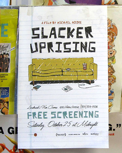 Promotional poster for the film “Slacker Uprising” by Michael Moore. The design resembles a sheet of lined notebook paper with hand-drawn elements, including a green couch surrounded by clutter like a soda cup, remote, and crumpled paper. Text at the bottom announces a free screening on Saturday, October 25 at midnight at Ken Cinema in San Diego. The background includes partial views of other colorful posters.