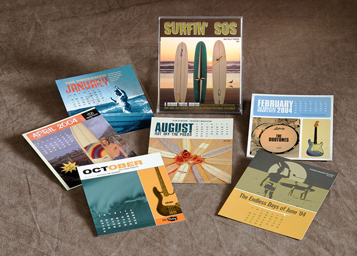 A collection of surf-themed calendar pages laid out on a brown fabric surface, with a main cover titled “Surfin’ SOS” featuring three surfboards on a beach at sunset. The individual monthly pages from 2004 include images of waves, guitars, surfers, and retro beach scenes, combining music and surf culture in a vibrant, nostalgic design.