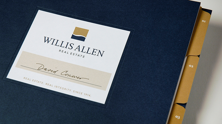 A navy blue binder for Willis Allen Real Estate featuring a clean, professional label on the front. The label includes the Willis Allen logo—featuring a gold and navy abstract square—along with the company name in serif font and the tagline “Real Estate. Real Integrity. Since 1914.” Below the logo, the name “David Conover” is handwritten on a beige strip. Gold index tabs numbered 01 to 03 are visible on the binder’s right edge, suggesting organized sections inside.