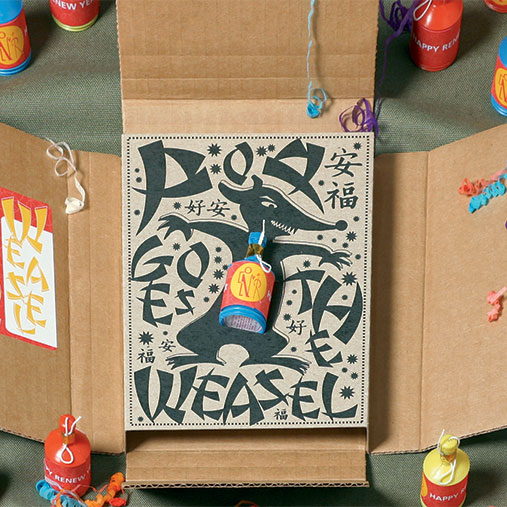 A playful, illustrated package design centered around the phrase “Pop Goes the Weasel,” featuring a stylized black weasel popping out of a box. The design is framed by cardboard packaging, with a small red and yellow party popper attached. Surrounding the main box are additional colorful poppers labeled “Happy Renewal,” placed on a green fabric surface, adding a festive and whimsical touch.