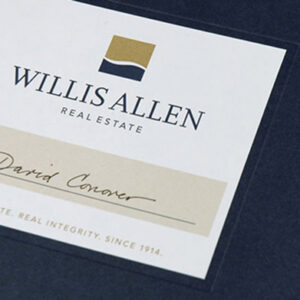 A navy blue binder for Willis Allen Real Estate featuring a clean, professional label on the front. The label includes the Willis Allen logo—featuring a gold and navy abstract square—along with the company name in serif font and the tagline “Real Estate. Real Integrity. Since 1914.” Below the logo, the name “David Conover” is handwritten on a beige strip. Gold index tabs numbered 01 to 03 are visible on the binder’s right edge, suggesting organized sections inside.
