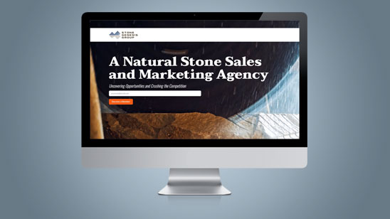 Computer monitor displaying the homepage of a natural stone sales and marketing agency, featuring a bold headline with an orange call-to-action button and a background image of stone textures and curved architectural elements.
